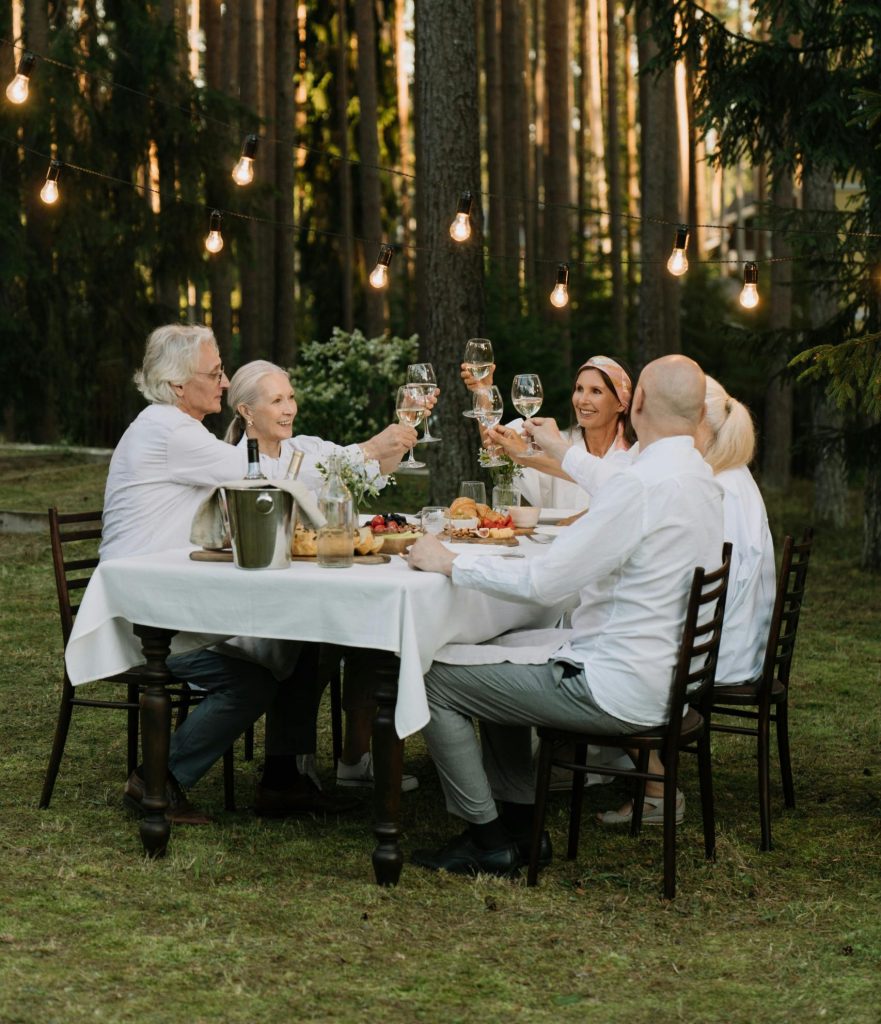 A group of friends toasting in a cheerful outdoor dinner setting surrounded by nature.