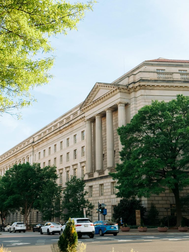 A classic government building with grand architecture in Washington, DC, surrounded by cars and trees.
